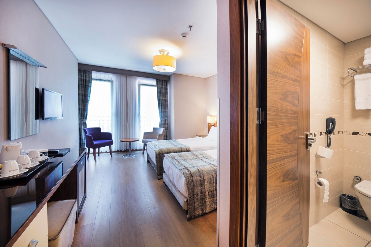Ein Hotelzimmer mit einem Bett, einem Schreibtisch mit Computer, einem Sessel, einem Fernseher und einem Badezimmer mit Toilette und Waschbecken.