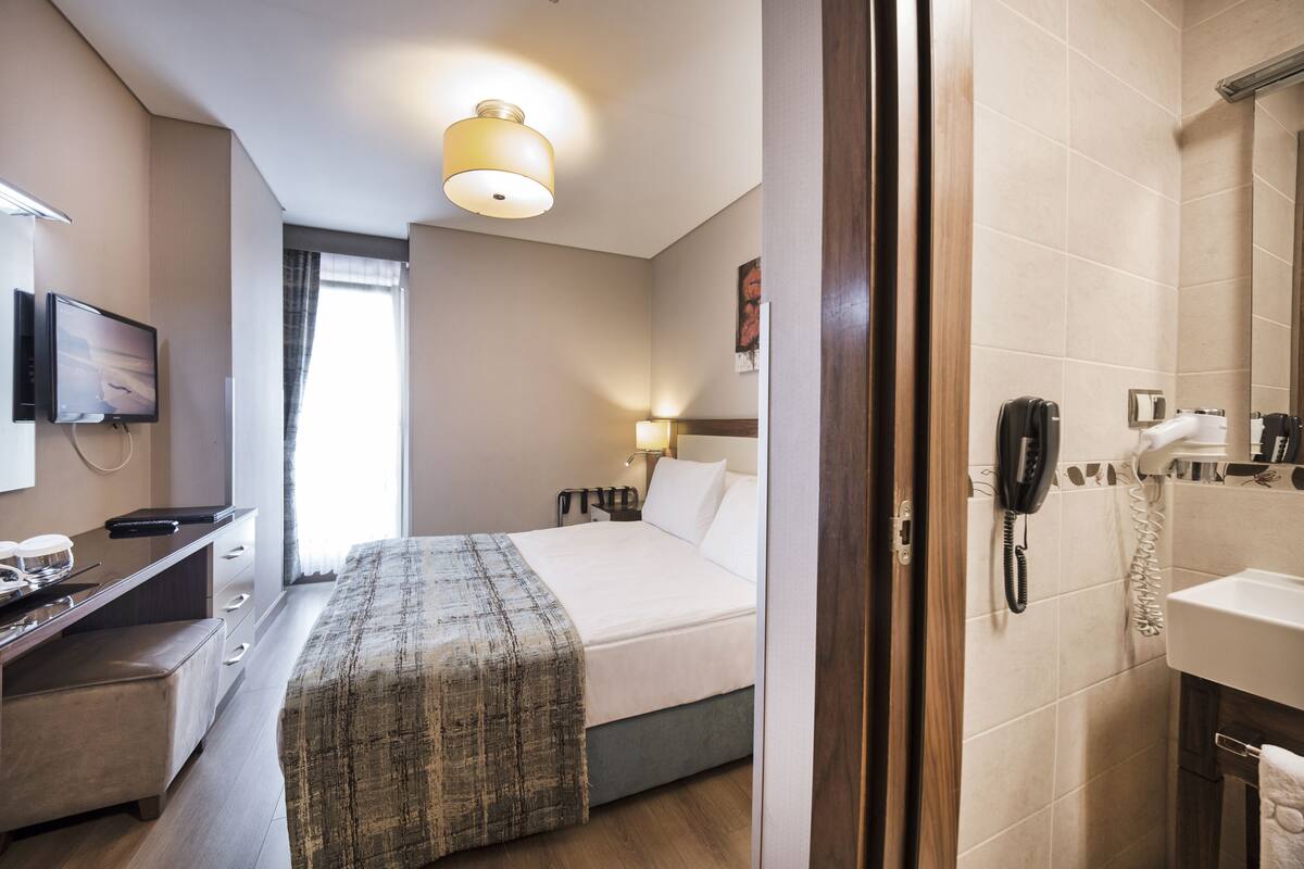 Een hotelkamer met een bed, nachtkastje, lamp en een bureau met stoel.