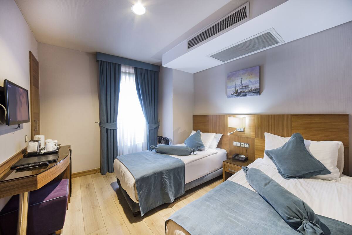 Een hotelkamer met twee bedden, een bureau met een computer, een televisie en een schilderij aan de muur.