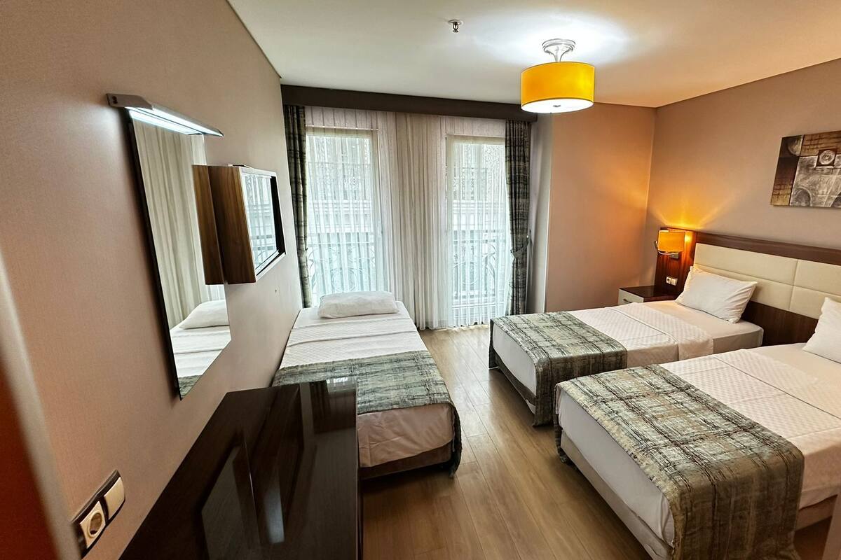 Een hotelkamer met twee bedden, een bureau, een spiegel, een lamp en een raam met gordijnen.