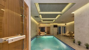 An indoor swimming pool with a glass enclosure, a lounge area with chairs, and a wooden door. - The Meretto Hotel İstanbul Old City (Istanbul)