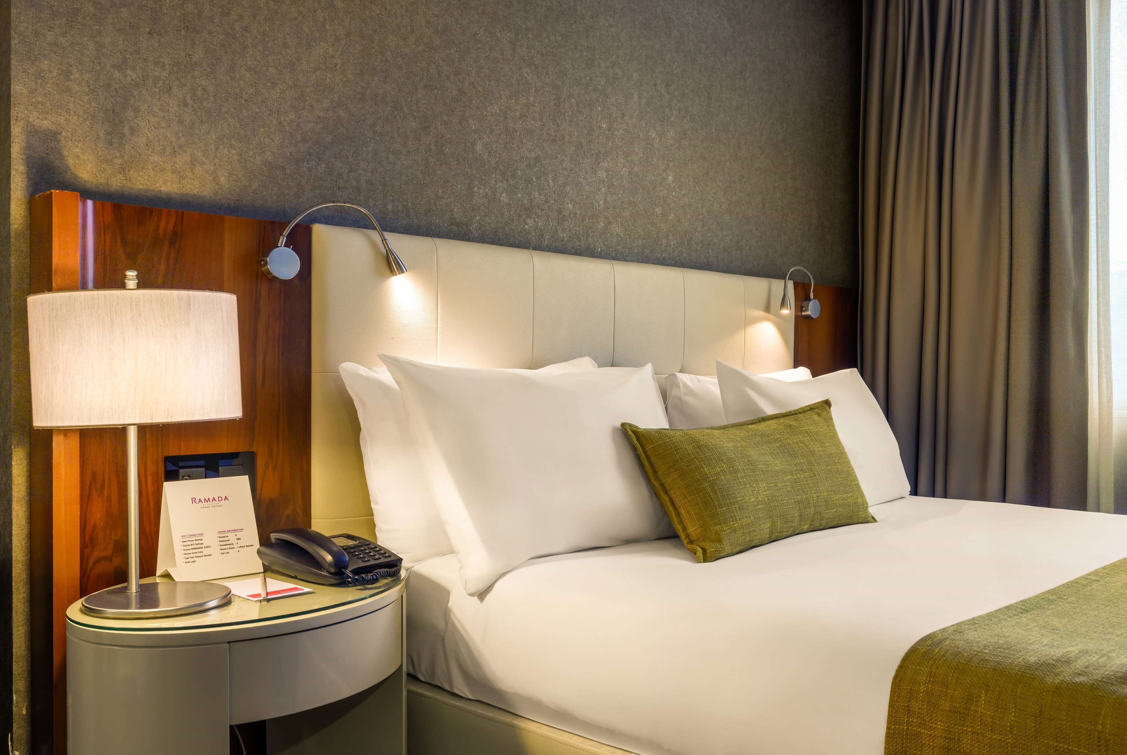 A hotel room with a bed, a bedside lamp, a telephone, and a sign indicating the room's name.