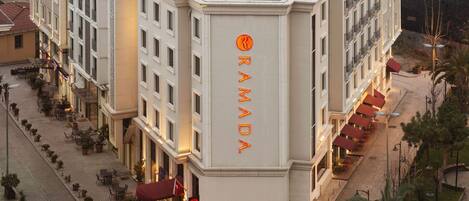 Un hotel con un llamativo letrero de 'RAMADA' en la esquina, mesas al aire libre y un patio empedrado.