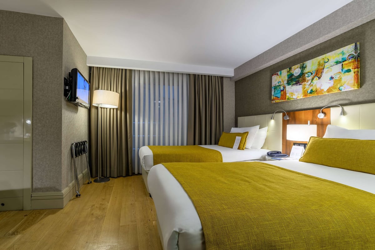 A hotel room with two beds, a TV, a painting, and a window with curtains.