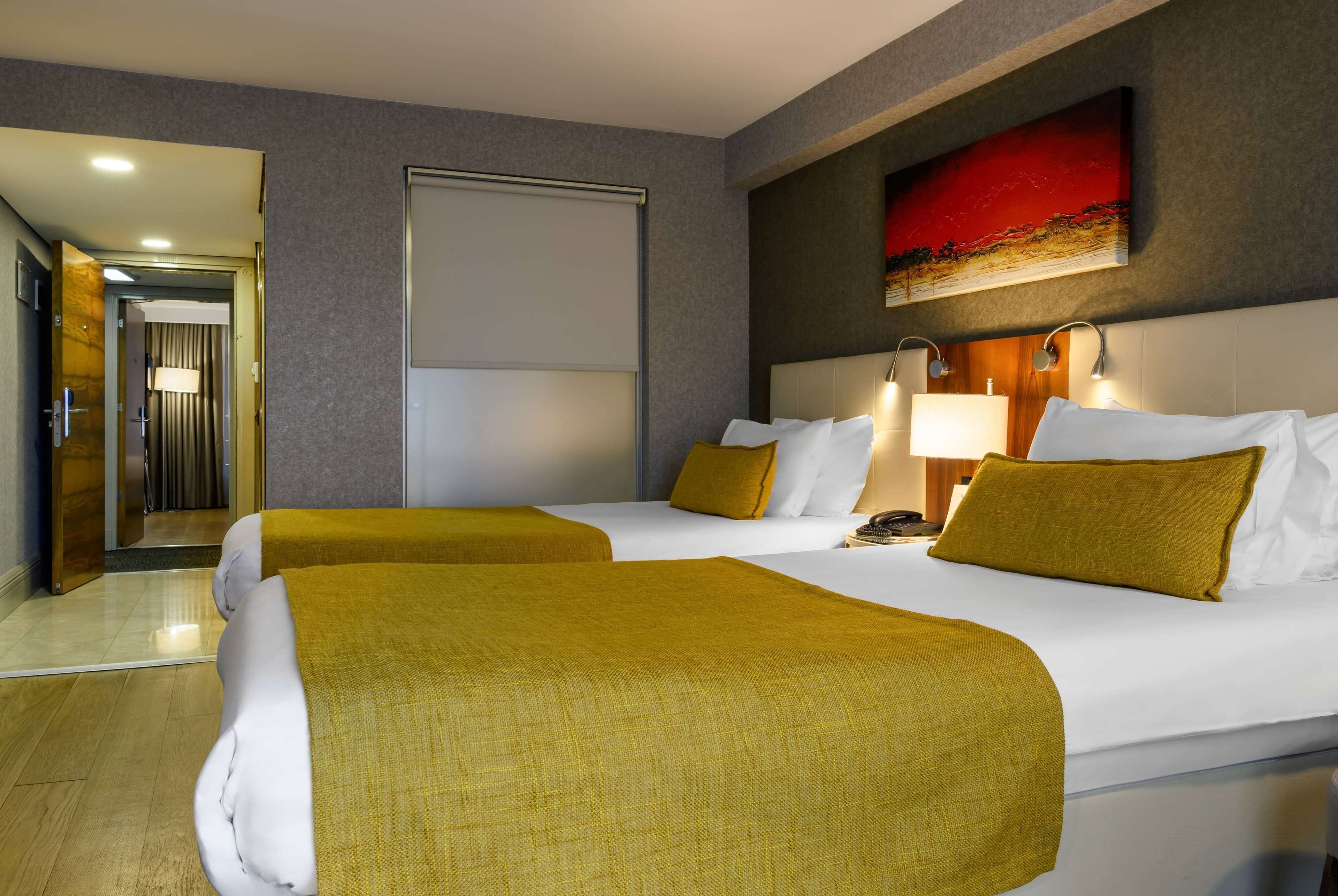 Une chambre d’hôtel avec deux lits, un grand tableau au mur et une porte donnant sur le couloir.