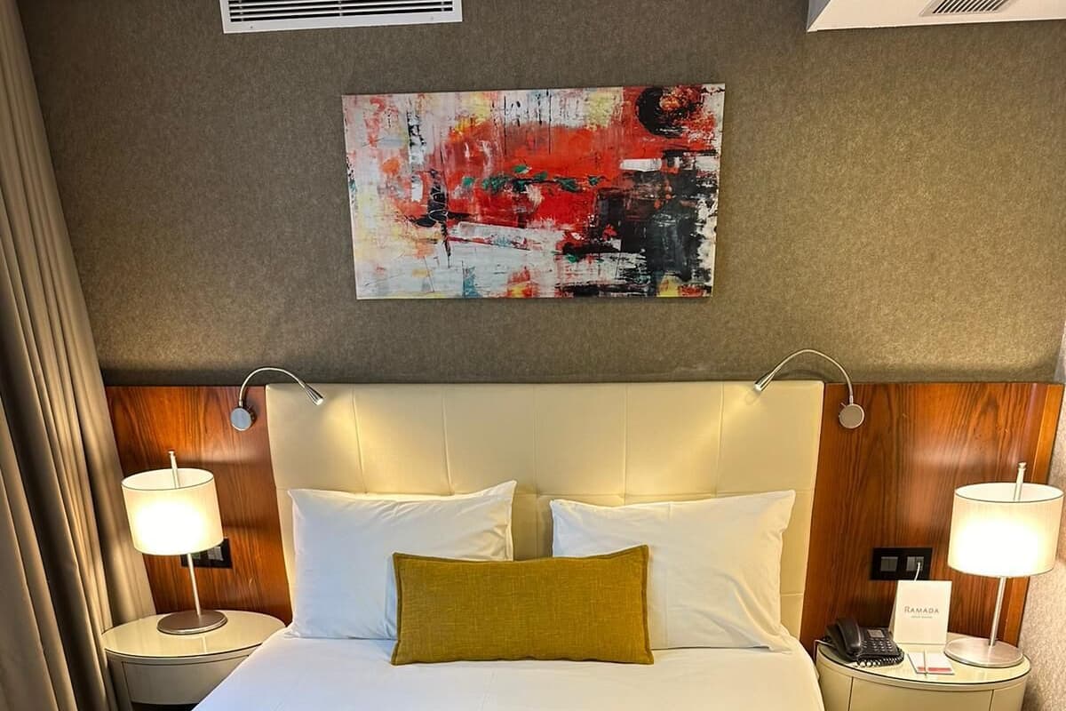 A hotel room with a large bed, two bedside tables with lamps, a wall-mounted artwork, and a sign indicating the room is for Ramadan.