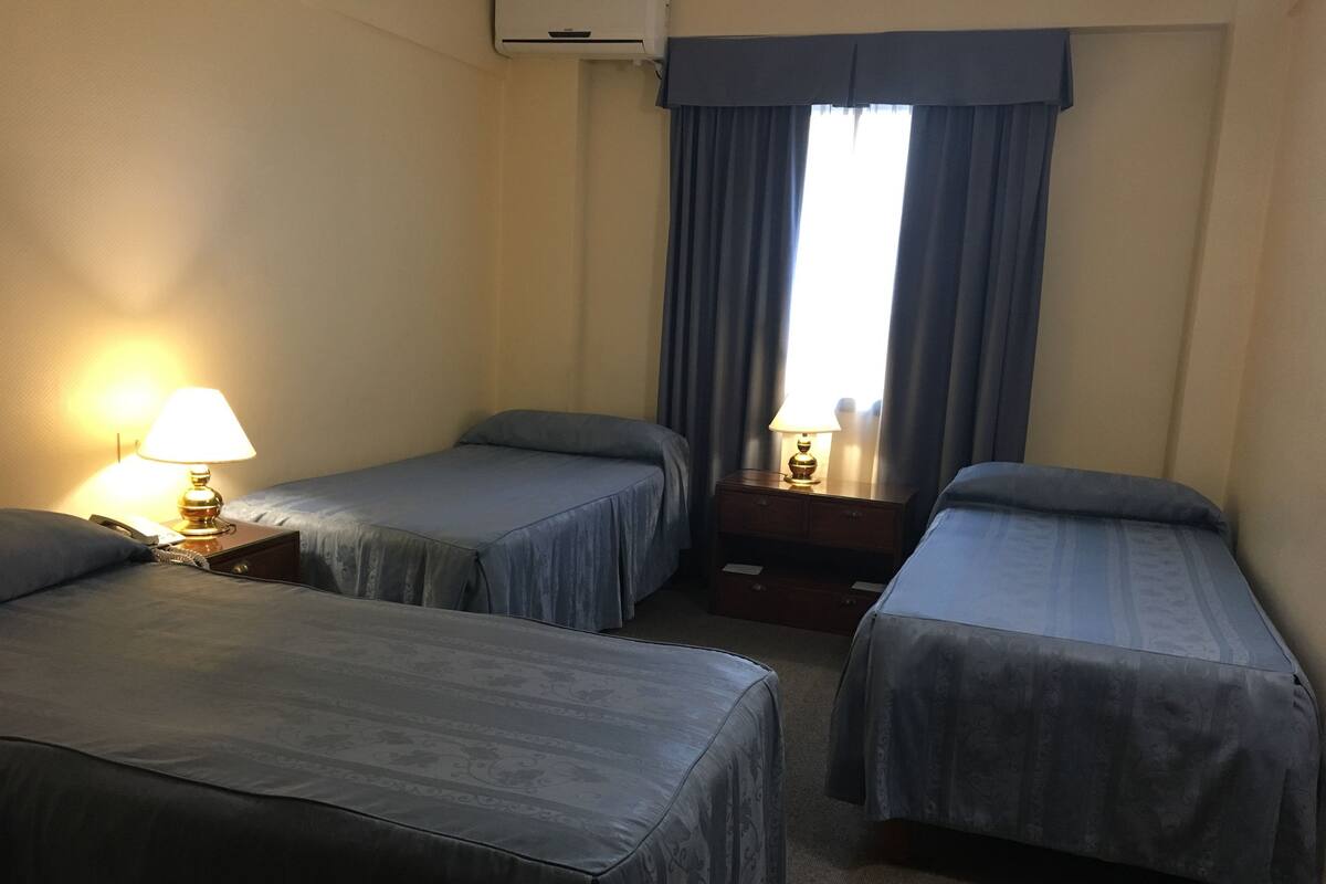 A hotel room with two single beds, a bedside table with a lamp, and a window with curtains.