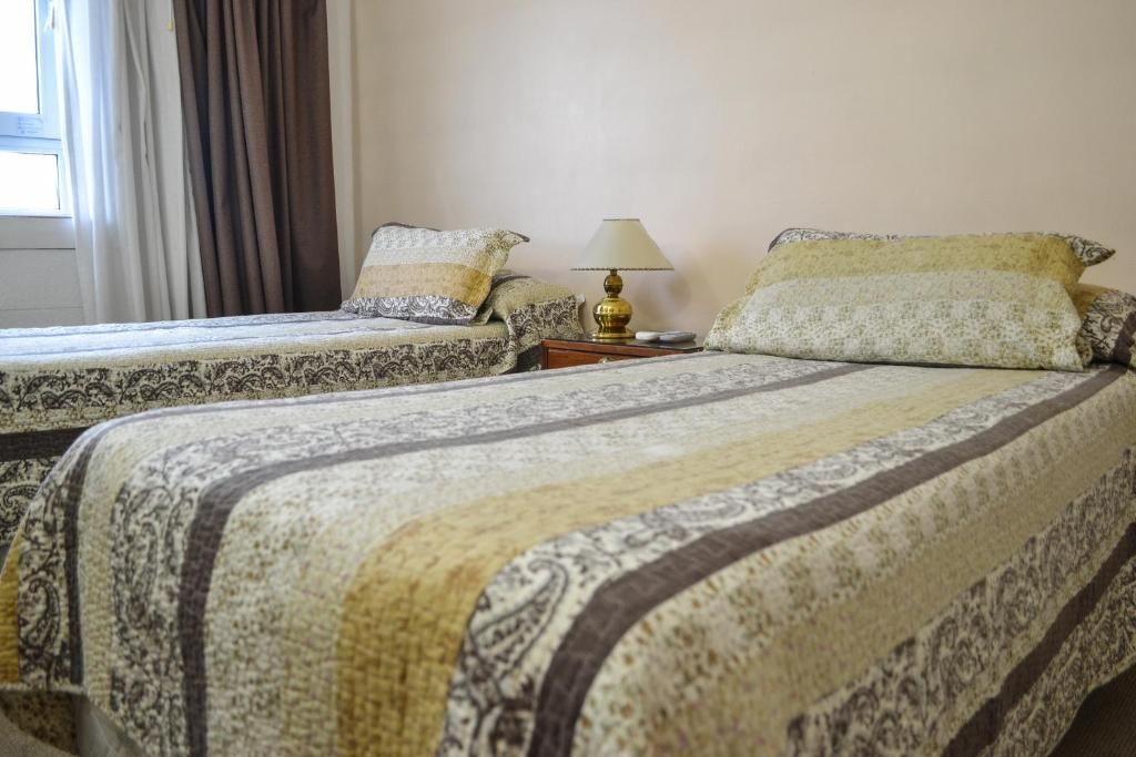 A hotel room with two beds, a nightstand with a lamp, and a window with curtains.