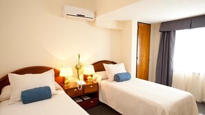 A hotel room with two beds, a bedside table with lamps, a phone, and an air conditioning unit. - Hotel Centro Naval (Buenos Aires)