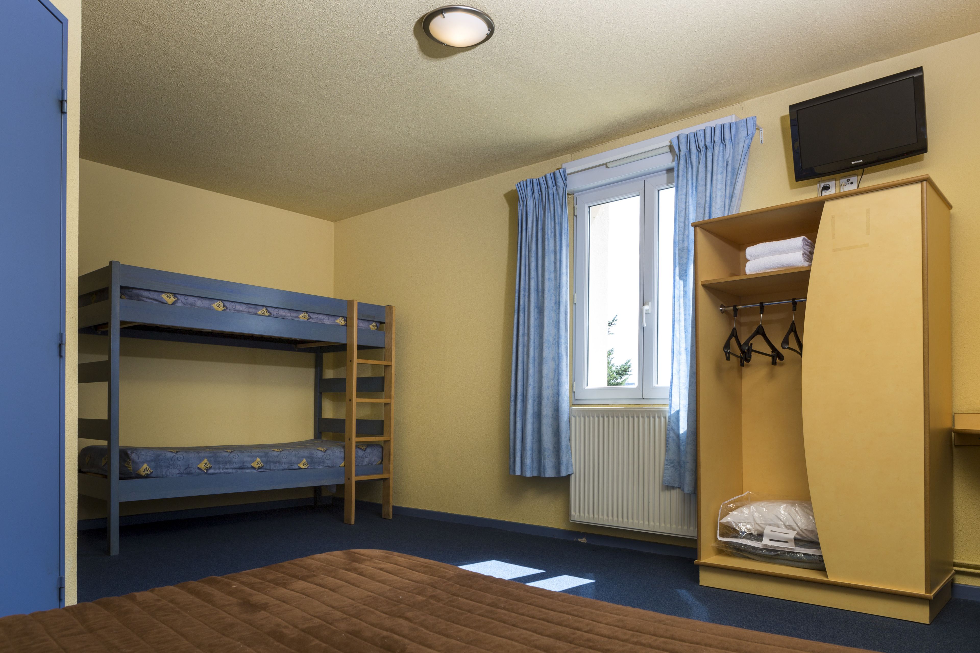 A room with bunk beds, a wooden wardrobe, a television, and a window with curtains.