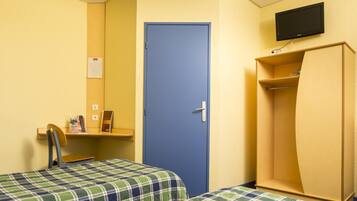 A room with two beds, a blue door, a television mounted on the wall, and a wooden wardrobe.