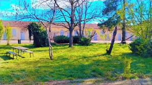 A courtyard with a picnic table and benches, surrounded by trees and a building with a tiled roof. - Hôtel & Résidence Avermes (Avermes)