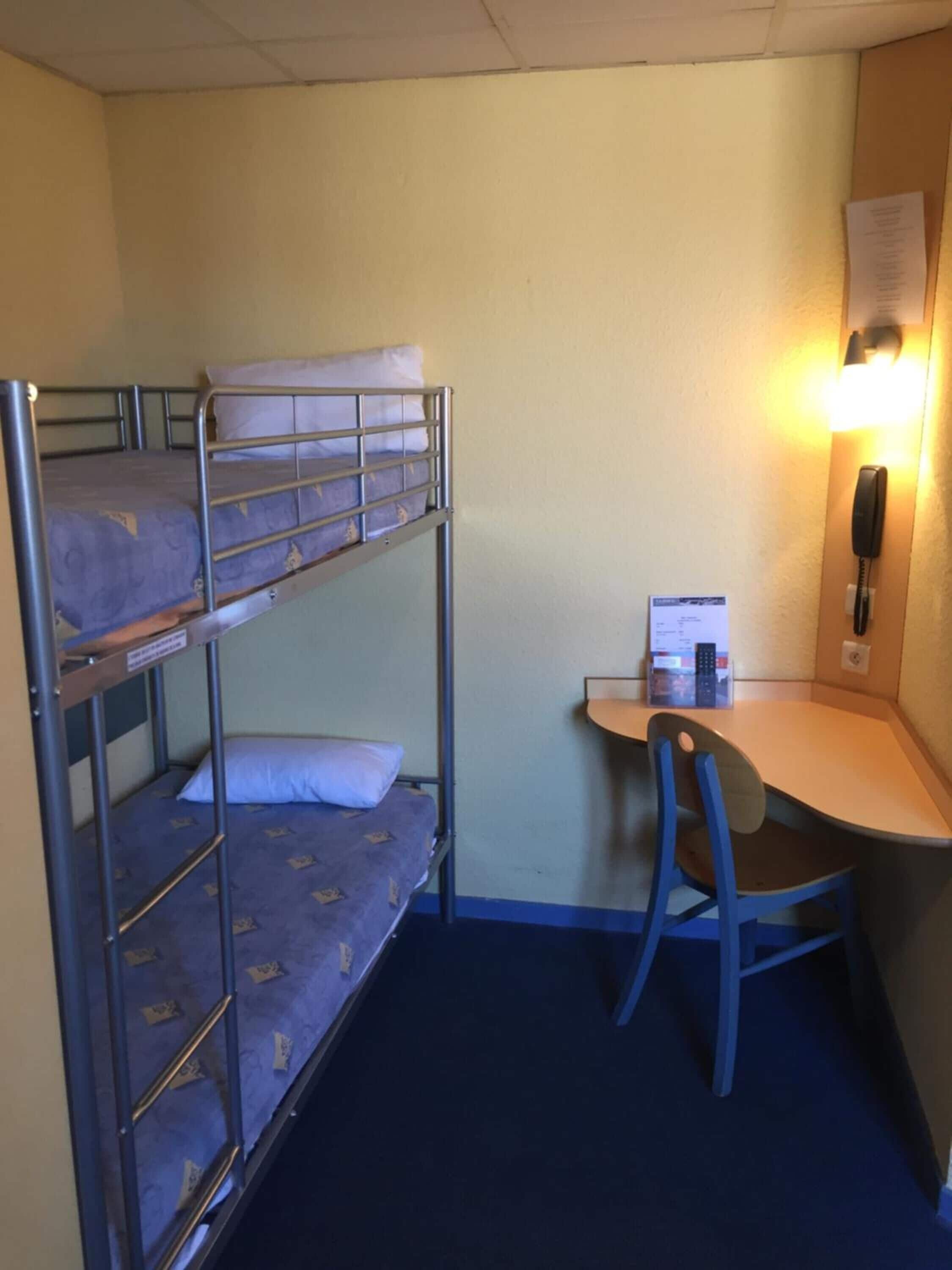 Une chambre avec un lit superposé, un bureau et une chaise, un téléphone et un luminaire.