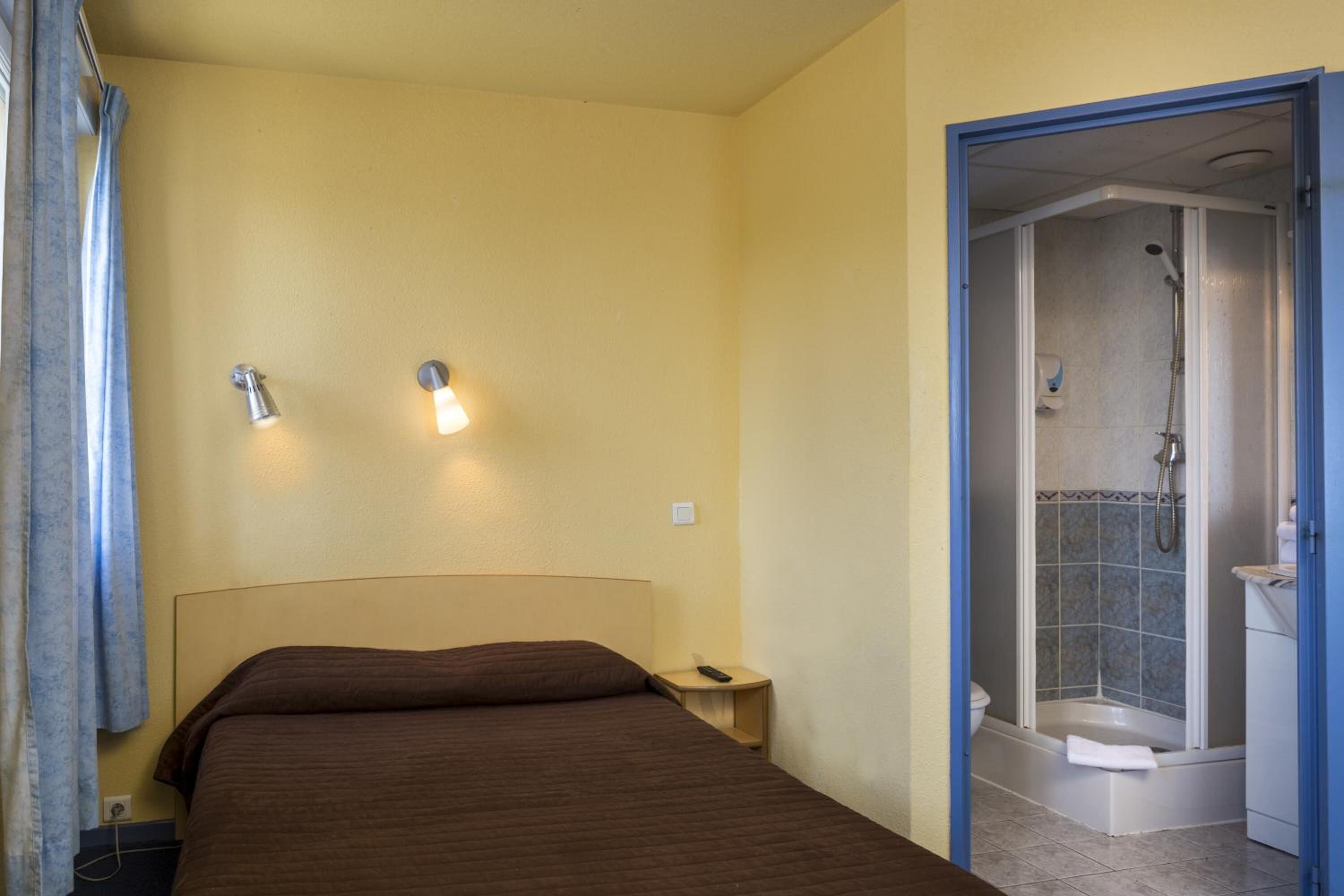 A hotel room with a bed, bedside lamps, a shower area, and a small bedside table.