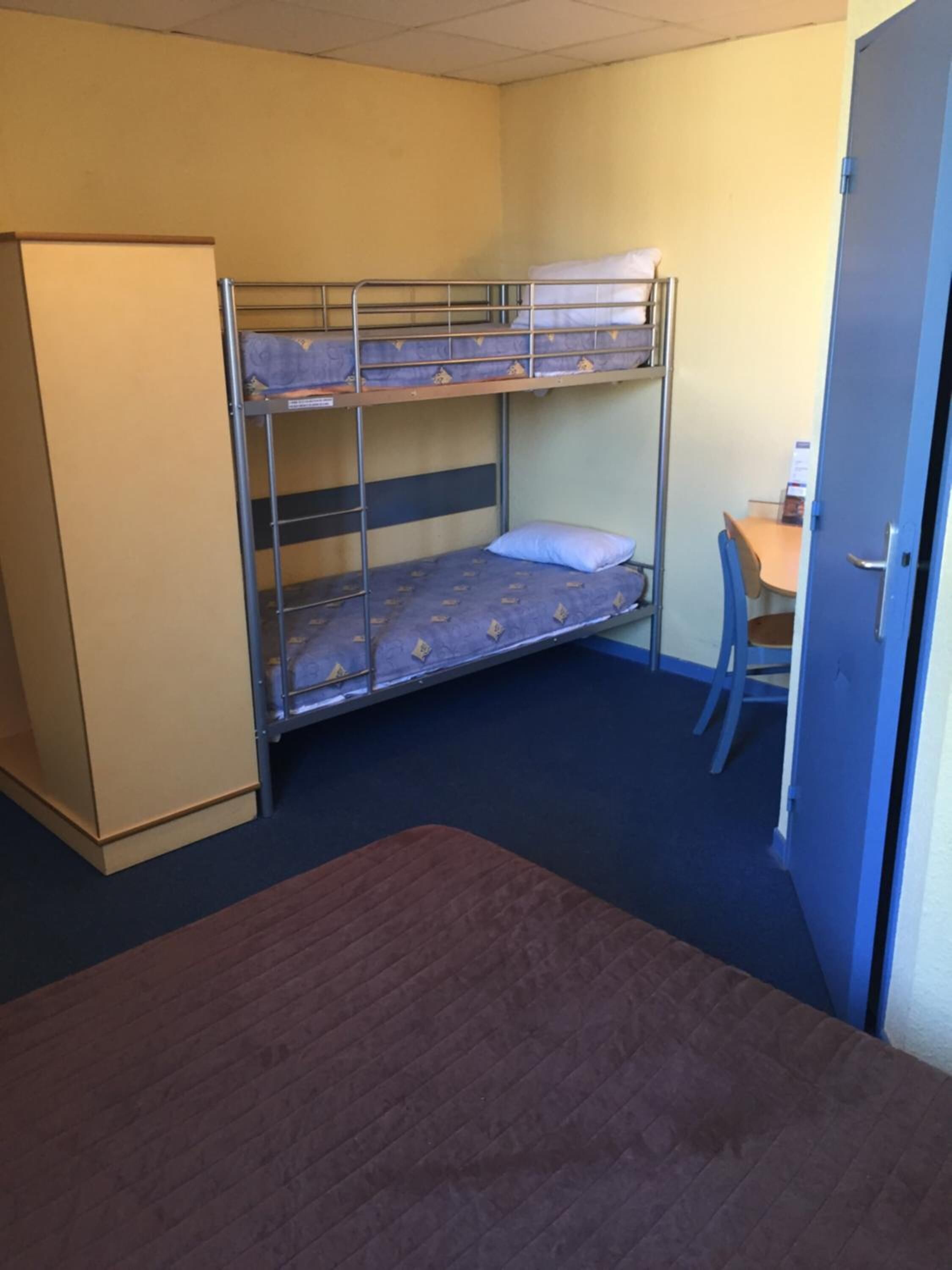 A bunk bed room with a desk and chair, a wardrobe, and a door.