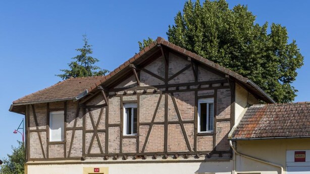 A two-story building with a traditional half-timbered facade, a parking lot with marked spaces, and a clear blue sky. - Hôtel & Résidence Avermes (Avermes)