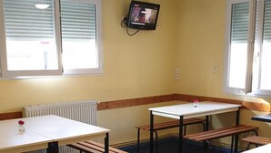 A room with four tables and benches, a television mounted on the wall, and windows with blinds. - Hôtel & Résidence Avermes (Avermes)