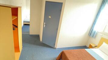 A hotel room with a bed, a wardrobe, a door, and a window with curtains.