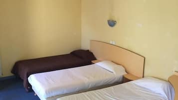 A room with two single beds, one with a brown bedspread and the other with a white bedspread. There is a small wall-mounted shelf above the beds.