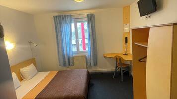 A hotel room with a bed, a desk, a chair, a television, and a wardrobe.