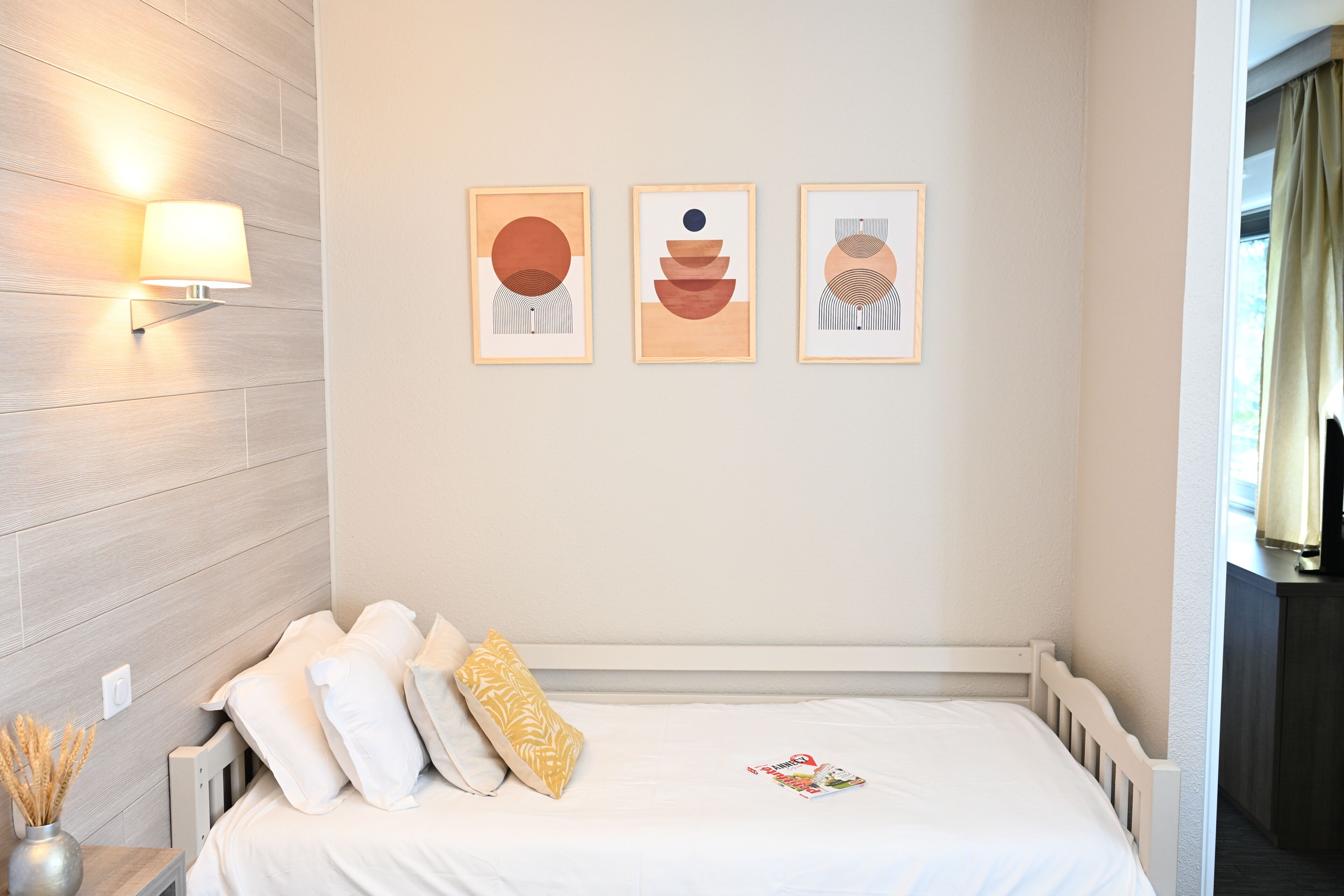 A hotel room with a bed, a wall-mounted lamp, and three framed artworks.