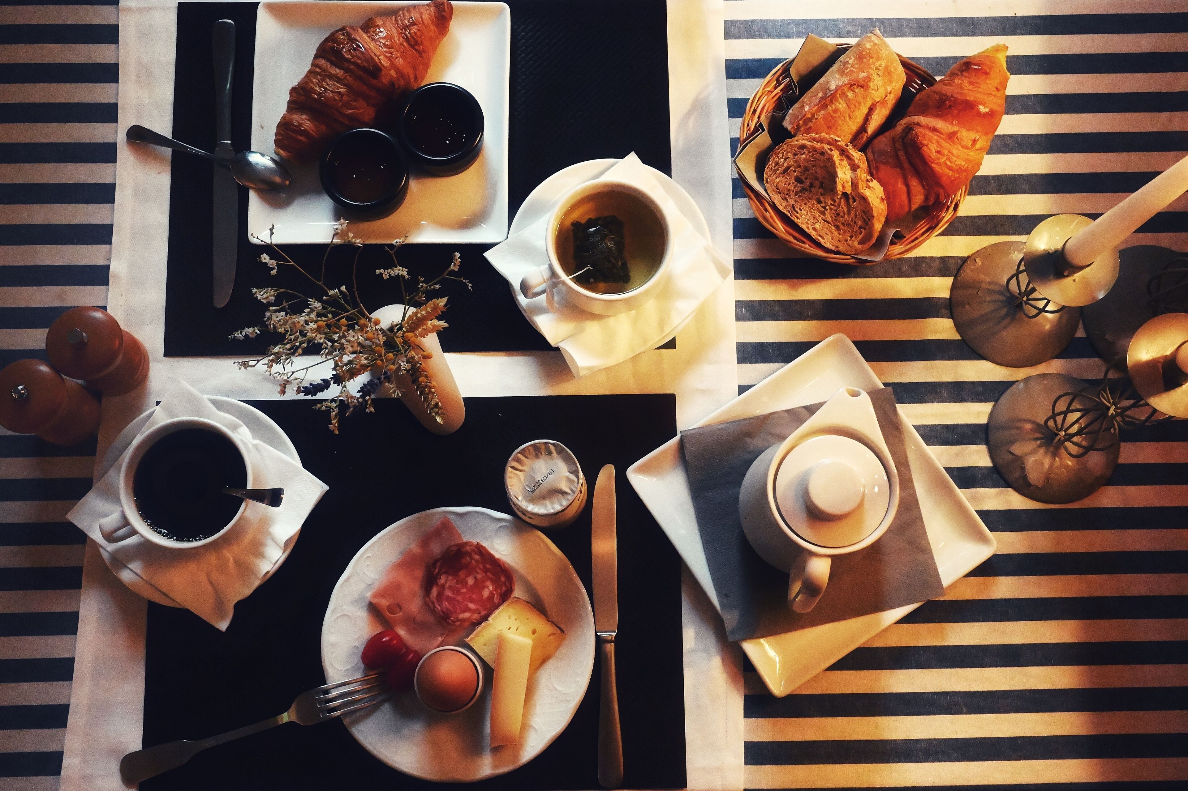 Una mesa con cruasanes, café, queso y un sándwich de croissant.