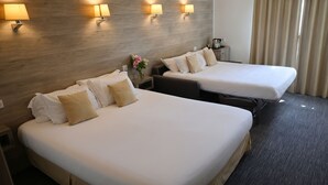 Een hotelkamer met twee bedden, een houten hoofdeinde, wandlampen, een nachtkastje en een vaas met bloemen.