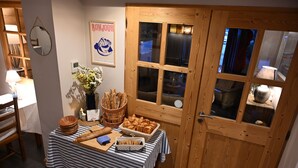 Een eetruimte met een tafel gedekt voor het ontbijt, inclusief brood, gebak en een vaas met bloemen.
