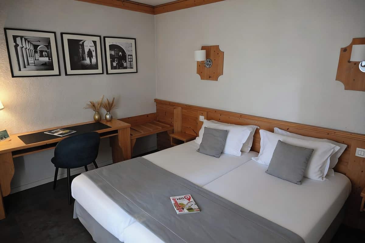 A hotel room with a bed, desk, chair, and three framed photographs on the wall.
