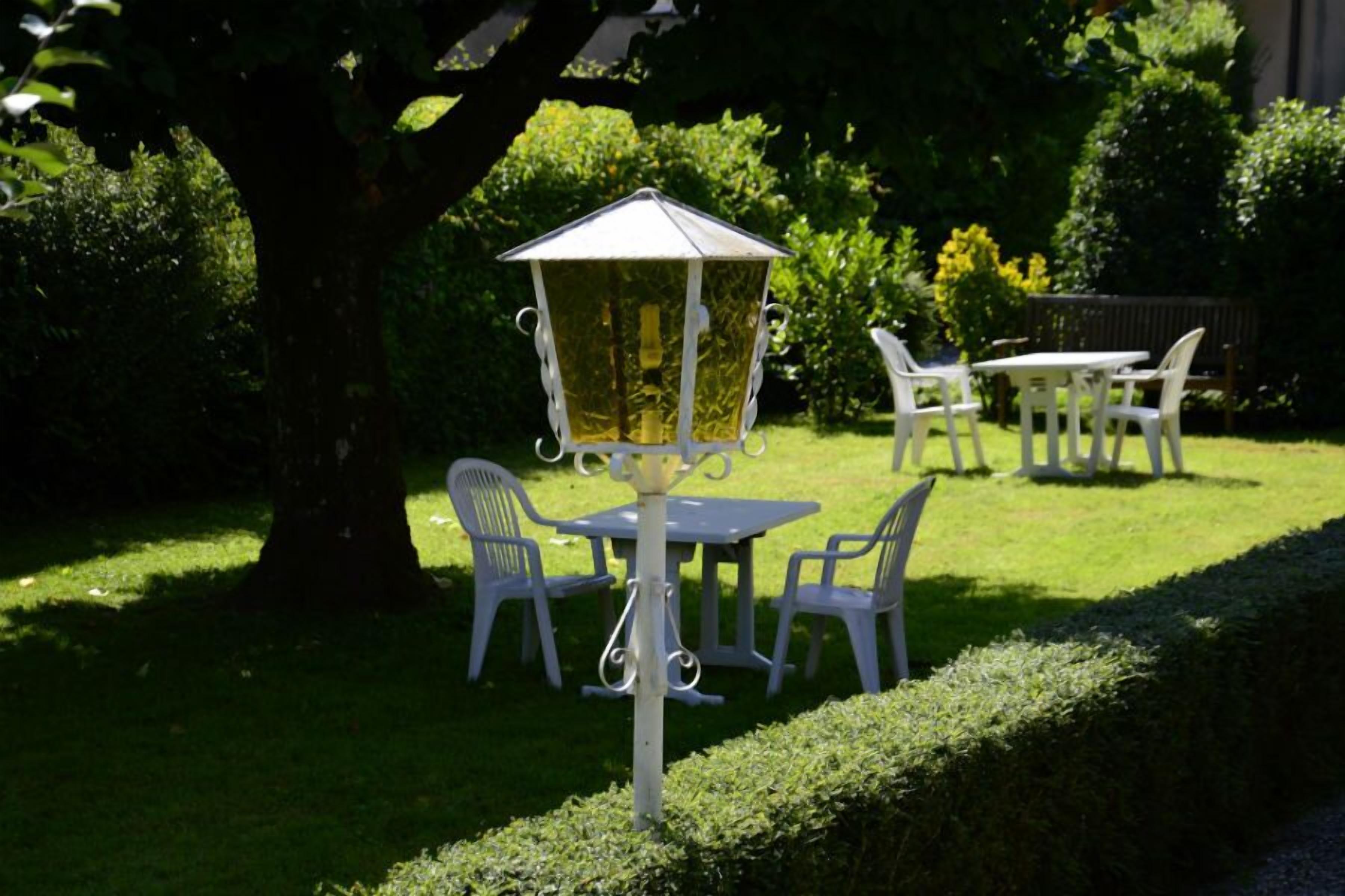 Un jardin avec une table et des chaises, un lampadaire et une haie.