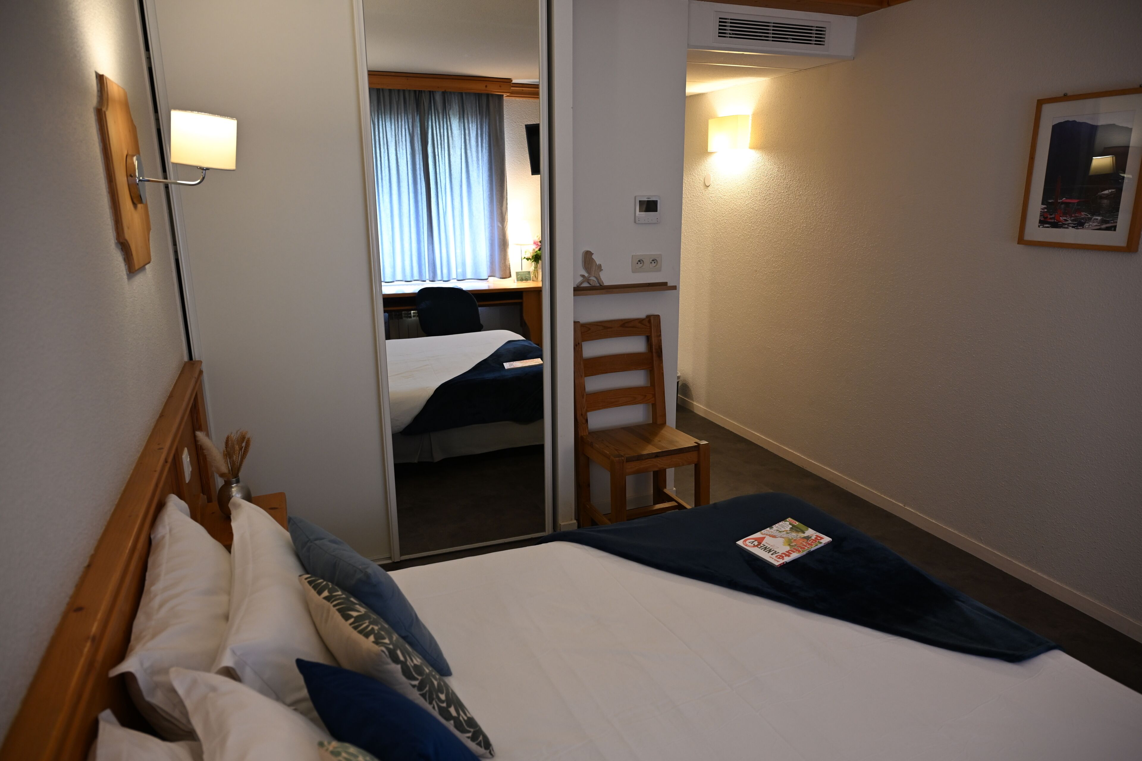 A hotel room with a bed, a chair, a desk, and a mirror.