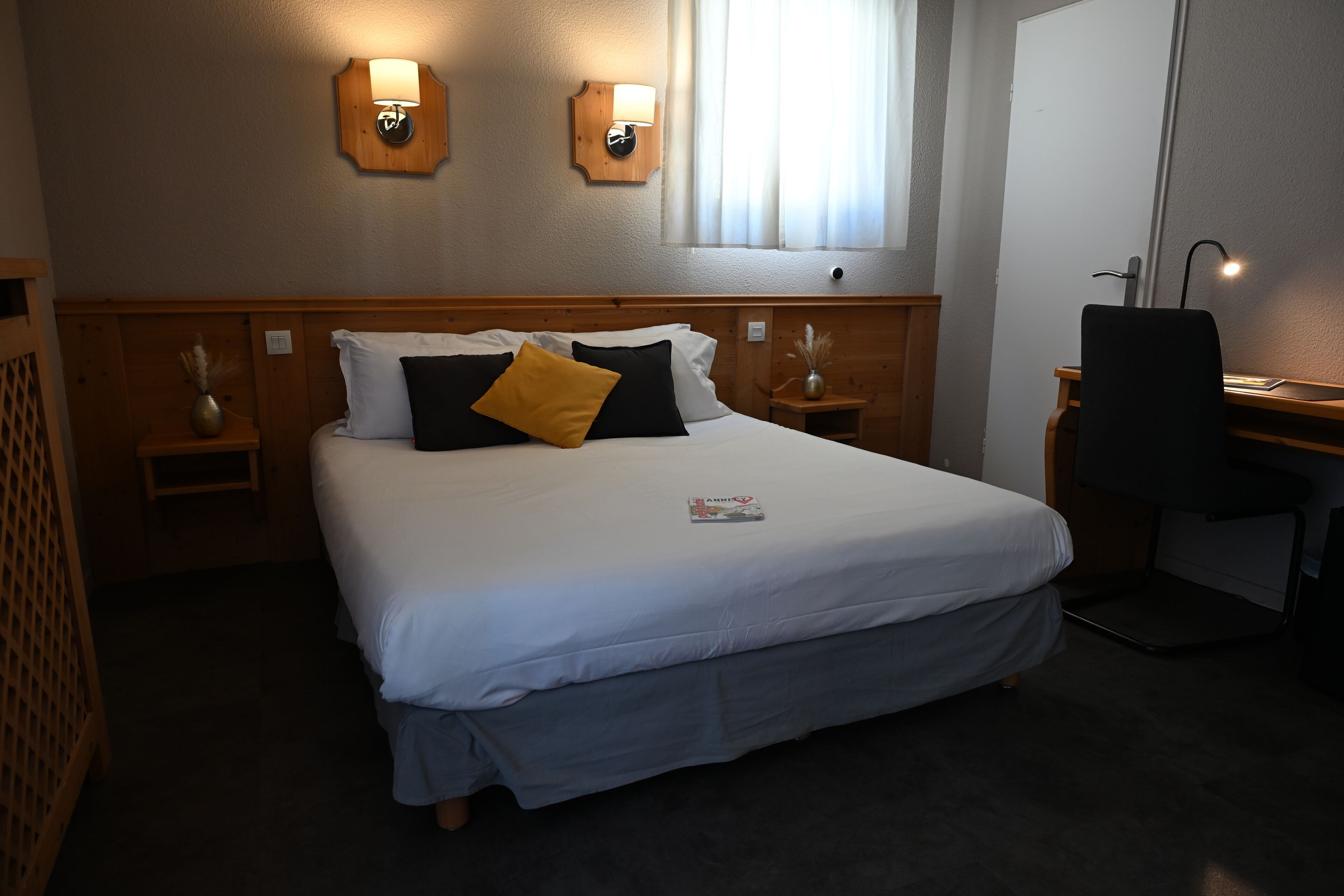 A hotel room with a bed, bedside tables, a desk, and a chair.