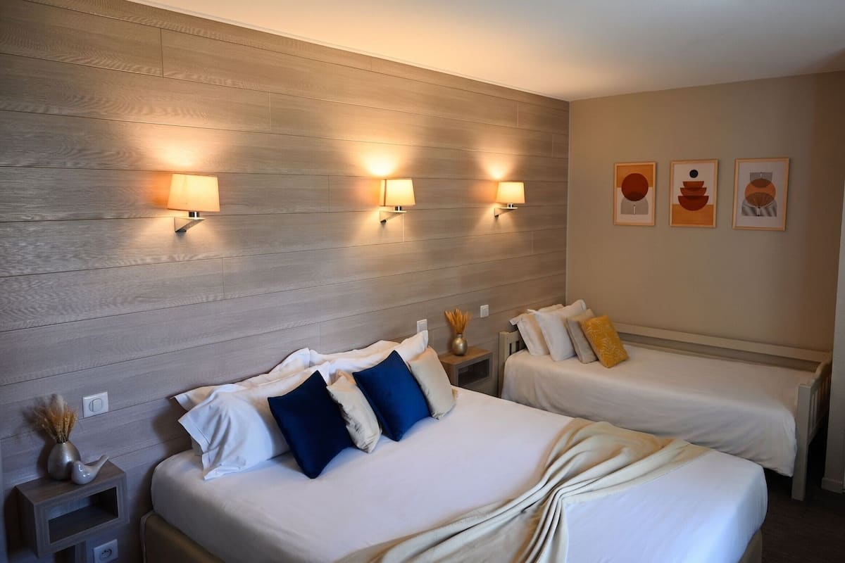 A hotel room with two beds, a wooden headboard, wall-mounted lamps, and framed artwork.