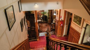 A staircase with wooden railings and a red carpeted floor leading to a room with a large plant, a statue, and a chair. - Le K'Loys (Paimpol)