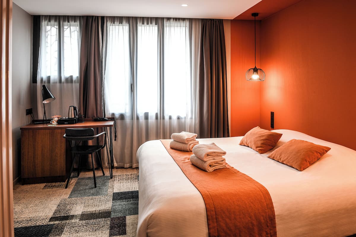 A hotel room with a bed, a desk with a chair, a coffee maker, and a lamp.