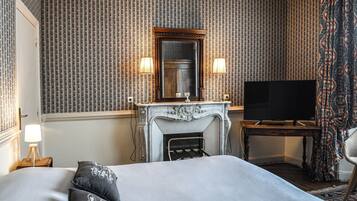 A hotel room with a large bed, a fireplace, a television, and patterned wallpaper.