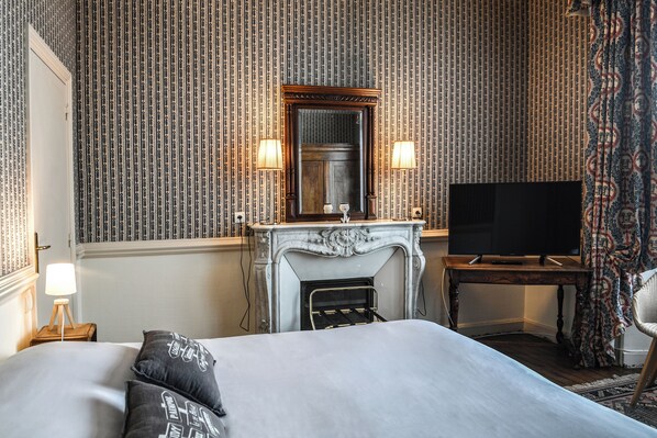 Una habitación de hotel con una cama grande, una chimenea, un televisor y papel tapiz estampado.