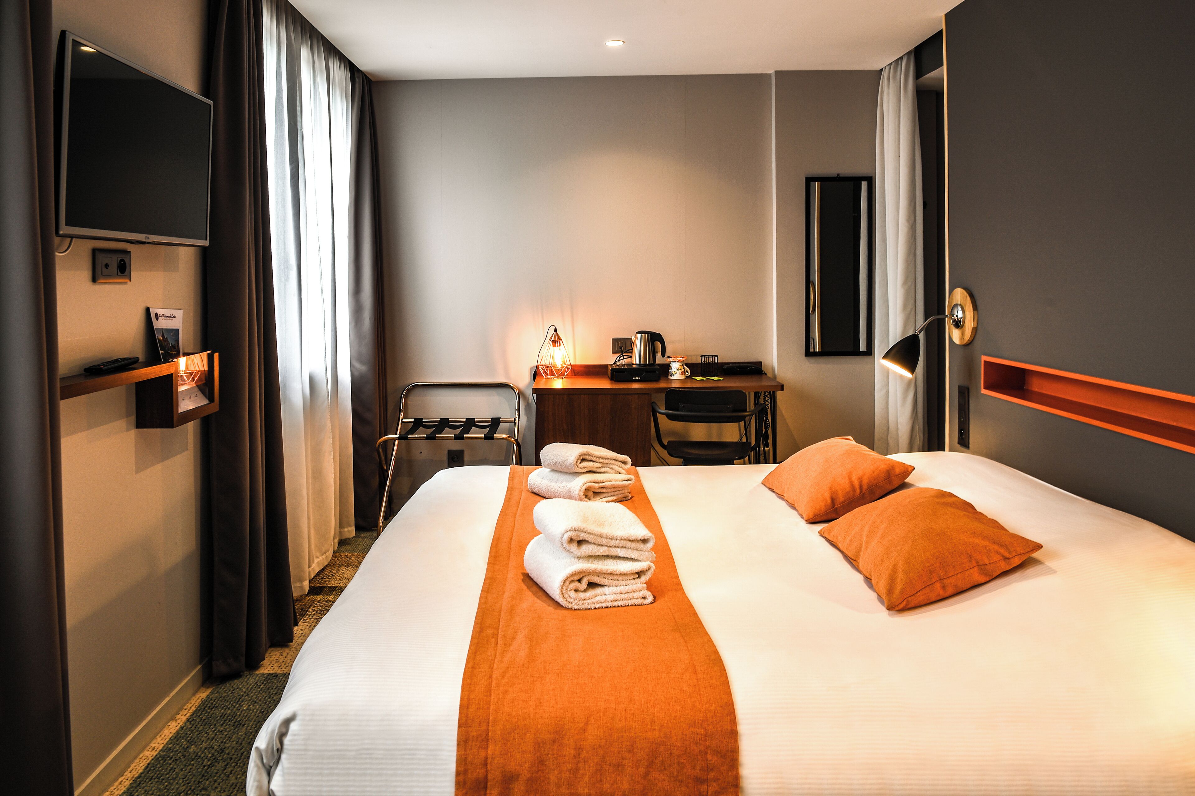 Habitación de hotel con una cama grande, un escritorio con silla, televisor y cafetera.