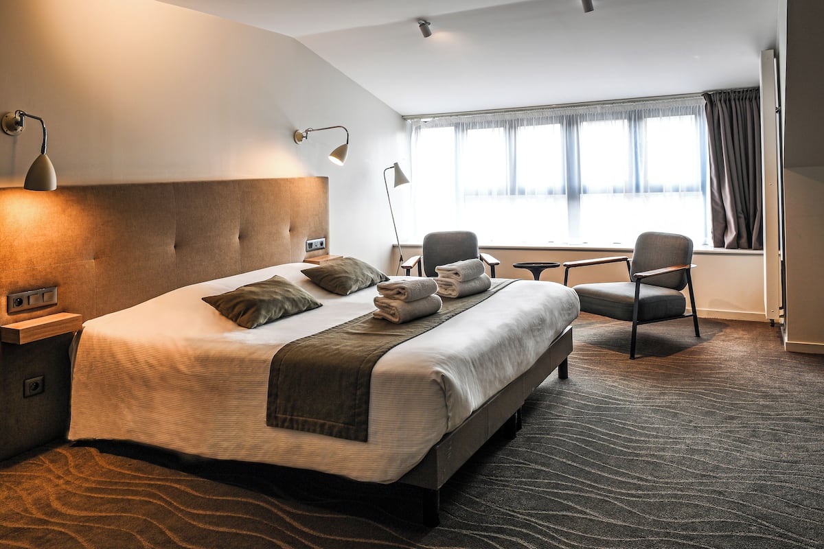 A hotel room with a large bed, two chairs, a desk, and a window with curtains.