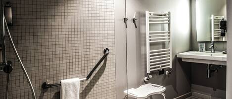 A bathroom with a shower, a sink, a mirror, a towel rack, and a step stool.