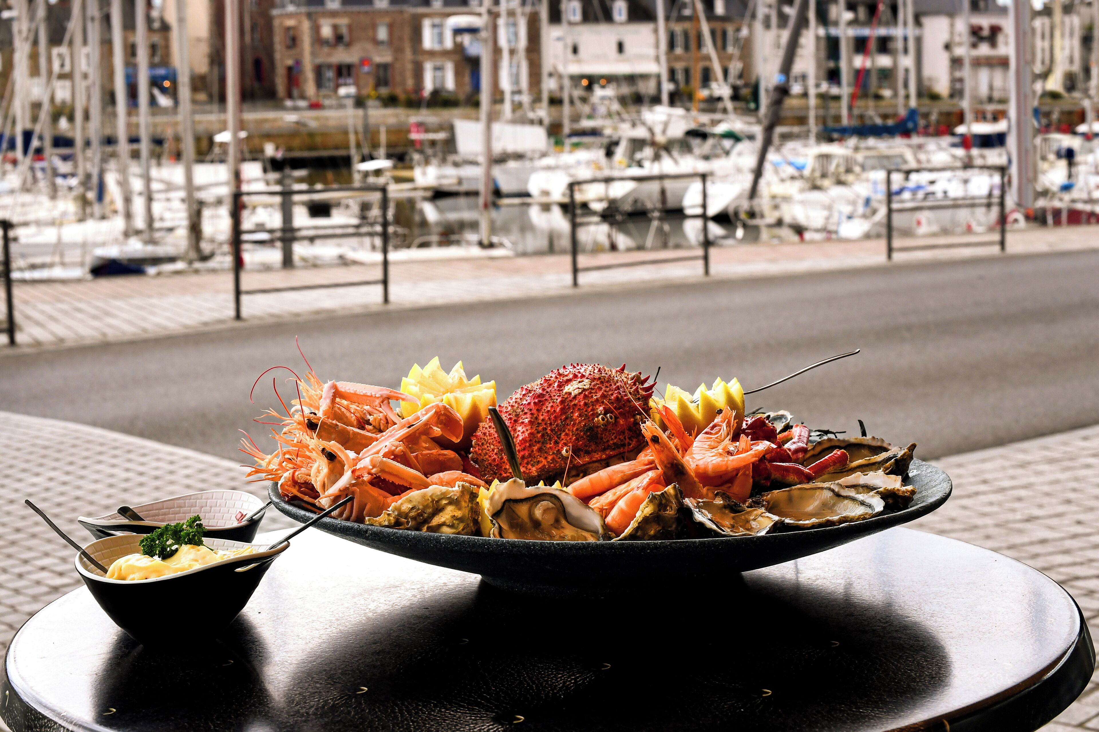 A seafood platter with shrimp, crab, and oysters on a table with a marina view in the background.