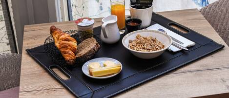 A breakfast tray with croissants, butter, granola, a glass of orange juice, and coffee cups on a wooden table.