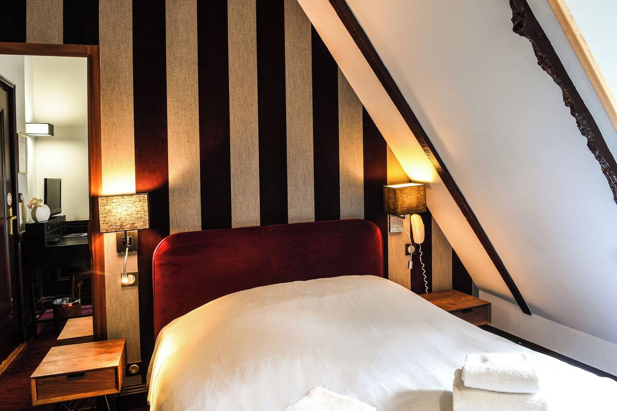 A hotel room with a large bed, striped wallpaper, and two bedside lamps.