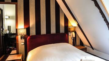 A hotel room with a large bed, striped wallpaper, and two bedside lamps.