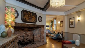 A room with a fireplace, wooden flooring, a sofa, and a chandelier.