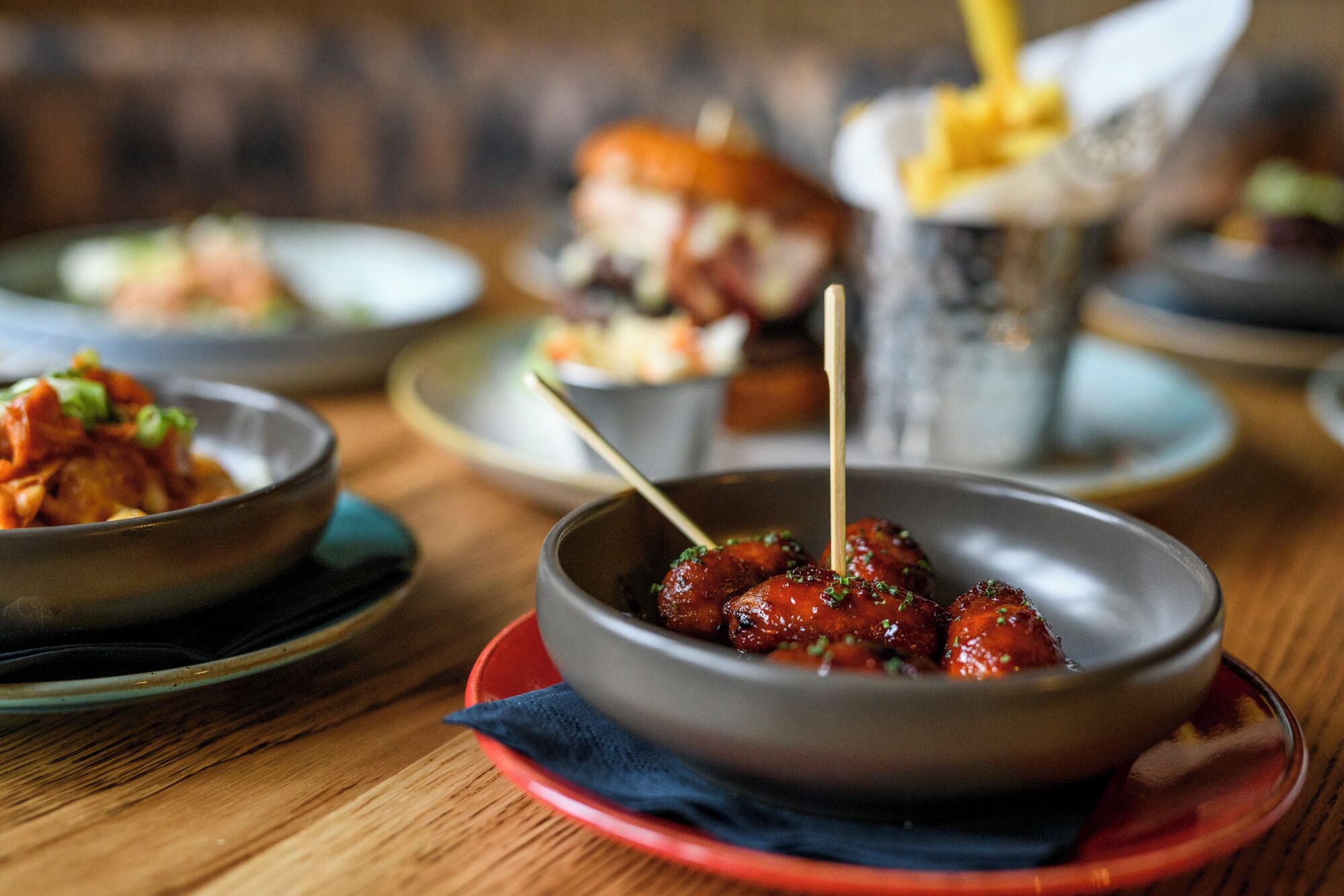 Une table à manger avec différents plats, notamment un plat de brochettes de viande, un hamburger et une portion de frites.