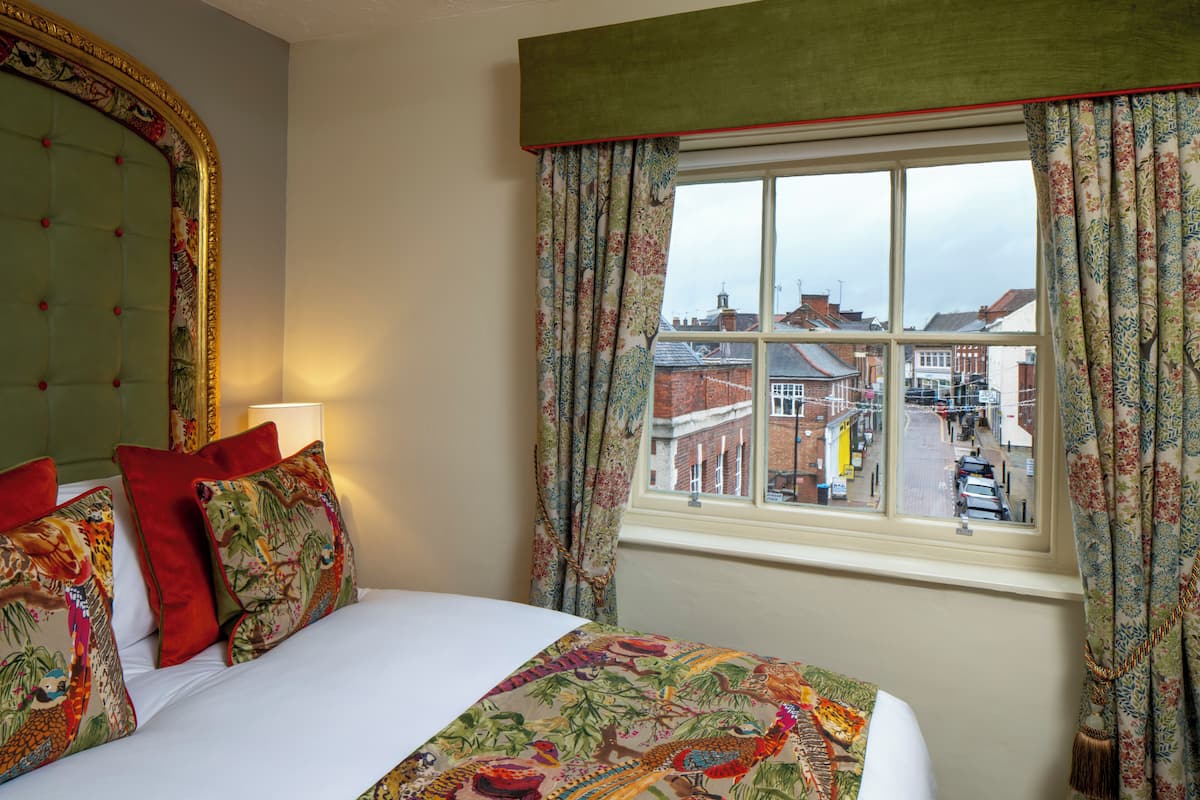 A hotel room with a bed, floral curtains, and a view of the street outside.