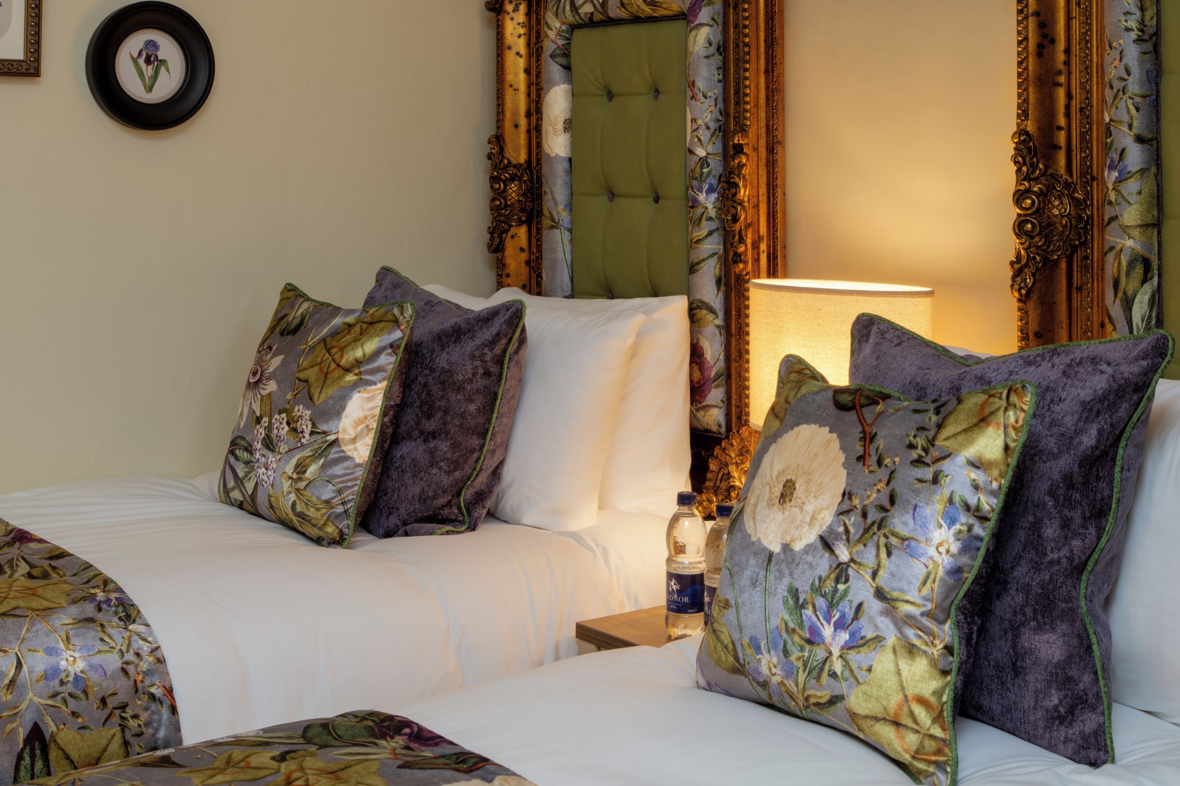 Una habitación de hotel con una cama, almohadas, una mesita de noche, una lámpara y un espejo.