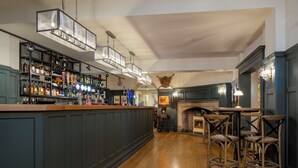 A bar area with a wooden floor, a bar counter with shelves of bottles, and a fireplace with seating.