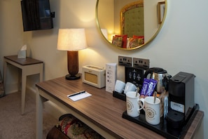 A hotel room with a desk, a lamp, a mirror, a coffee maker, and a television.